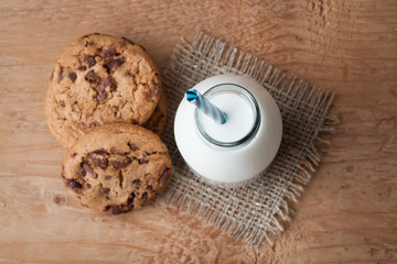 Bottle with milk and chocolate chip cookies on dark background. Top view