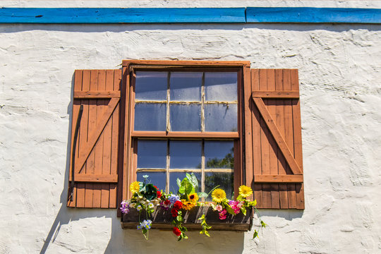 Colorful and pictureque dusty window with shutters and flowers in windowbox with shutters in white stucco wall with blue wood trim