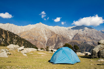 A single blue tent seen against Dhaulahaar peaks of Himalayas in Triund. Sunny day whit some clouds. Dharamshala, Himachal Pradesh. India