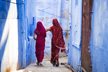 Two women dressed in the traditional Indian Saree are walking through the narrow streets of the blue city of Jodhpur, Rajasthan, India.