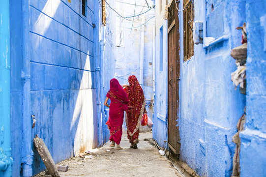 Two women dressed in the traditional Indian Saree are walking through the narrow streets of the blue city of Jodhpur, Rajasthan, India.