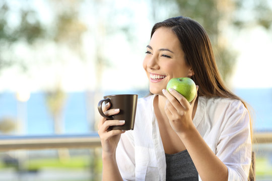 Happy woman holding an apple and a coffee mug