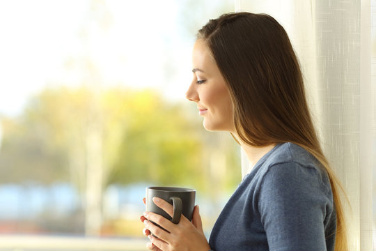 Pensive lady holding a coffee mug beside a window