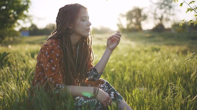 beautiful hippie woman with dreadlocks in green grass at sunset having good time outdoors