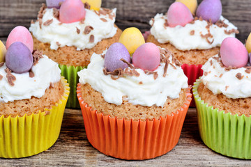 Little easter cupcakes with easter eggs and frosting on wood background