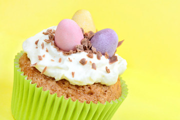 Easter cupcake with chocolate eggs on yellow background