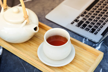 Hot tea is in a glass on a wooden traynear computer.