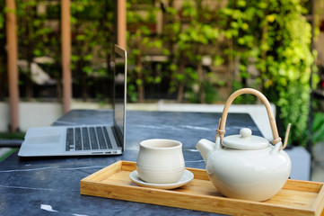Hot tea is in a glass on a wooden tray near computer.