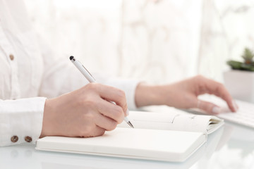 Close up of female hands writing and using computer, high key. Blogger or business concept