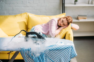 iron burning on shirt while woman sleeping on sofa at home