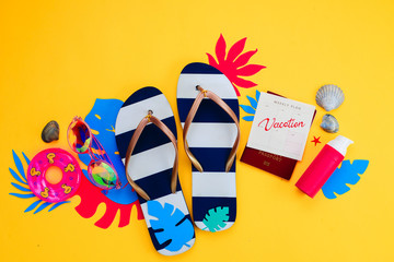 Summer holiday concept, travel and beach accessories with copy space. Flip flops, tropical leaves and a calendar with Vacation note on a vibrant yellow background.