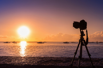 silhouette of camera on tripod shooting sea with sunset.