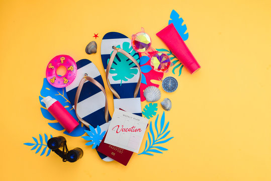 Summer vacation accessories, sunglasses, flip-flops, sunscreen, tiny swim ring, shells on a vibrant yellow background. Traveling essentials flat lay with copy space. Feminine blue and pink palette.
