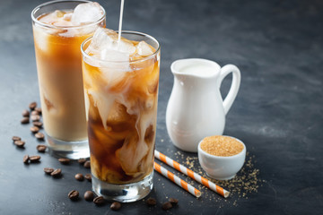 Ice coffee in a tall glass with cream poured over, brown sugar and coffee beans. Cold summer drink...