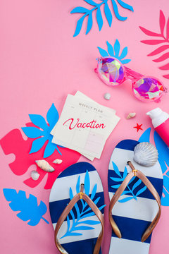 Flip flops, sunglasses and sunscreen on a vibrant pink background with copy space. Feminine summer vacation essentials concept. Colorful travel flat lay with tropical leaves.