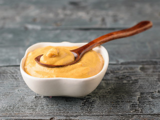 Freshly made mustard seed sauce in a white bowl on a rustic table with a spoon.