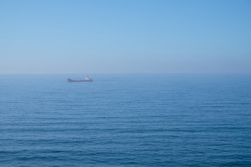 Cloudy horizon and Fog over the sea waves, natural background, red cargo ship on the horizon