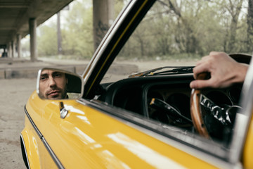 cropped shot of bearded man reflected in mirror of yellow classic car