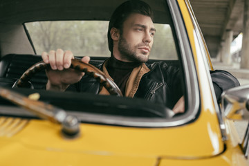 pensive handsome stylish man sitting in vintage car and looking away
