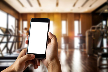 A man hand holding smart phone device in the fitness room view background in morning light
