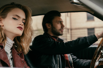 attractive stylish girl looking at camera while handsome boyfriend driving car