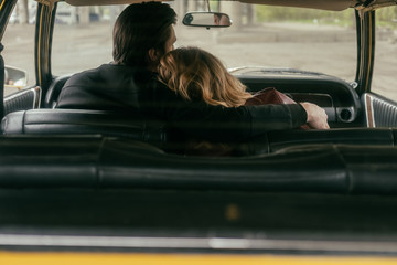 back view of young couple in love embracing while sitting together in car