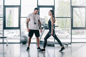 male personal trainer looking at sportswoman exercising with dumbbells at gym