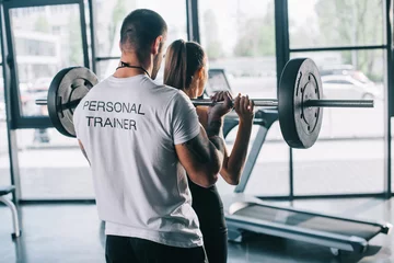 Foto op Aluminium male personal trainer helping sportswoman to do exercises with barbell at gym © LIGHTFIELD STUDIOS