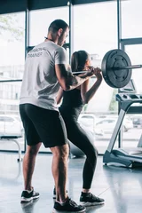 Fotobehang male personal trainer helping sportswoman to do exercises with barbell at gym © LIGHTFIELD STUDIOS
