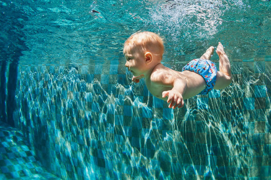 Happy child learn to swim, dive in blue pool with fun - jumping deep down underwater with splashes. Healthy family lifestyle, kids water sports activity, swimming lesson with parents in fitness club