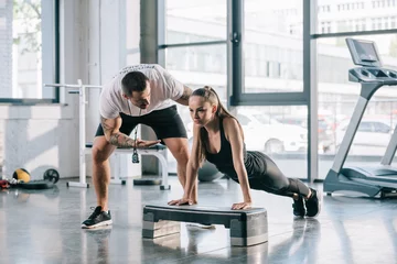 Fotobehang male personal trainer helping sportswoman to do push ups at gym © LIGHTFIELD STUDIOS