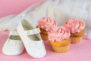 Baptism or birthday girl invitation with pink cup cakes and white shoes on pink background