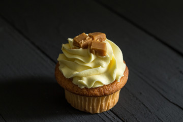 One single caramel frosted cup cake with fudge square decoration on top, isolated on black wooden...