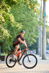 Fototapeta premium Toned sportsman cycling on bicycle near green park. Cyclist shooting for clothing advertisement campaign. Concept of healthy lifestyle, sport advertising, outdoor activities