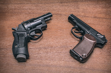 Two air guns - pistol and handgun (revolver) on wooden table surface background. Shooting practice.
