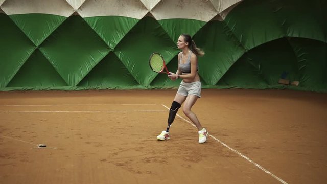 Backside view of energetic young woman with a prosthesis down her knee is focused on beating the ball on an elastic band. Indoors