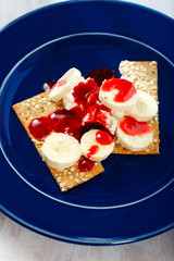 Dessert with dietary cookies, banana, raspberry topping and cream cheese mascarpone in blue plate on white wooden table. Healthy food