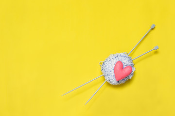 Top view of yarn and red felt heart on yellow background, love to knit image concept