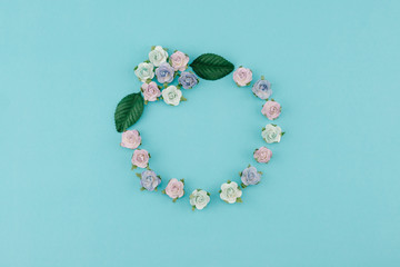 Round wreath made from blue tone paper flowers and green leaves on pastel blue background with copy space