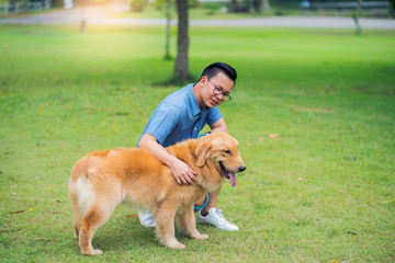 Smiley man in the blue shirt play with lovely golden retriever dog in the garden