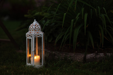 cozy evening garden scene with vintage lantern and candle holder with lawn and flowers on background
