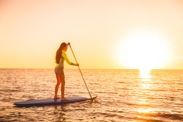 Sporty girl stand up paddle surfing with beautiful sunset or sunrise colors