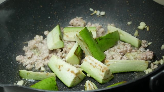 put green sliced piece eggplants into the  pan ,  fried sliced garlic , food palm  oil and minced pork , stir fried together in the black teflon pan with two wooden turners,