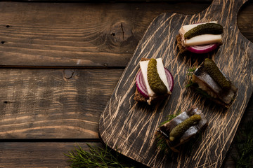 Mini sandwiches with bacon and herring as a snack to vodka on a dark background