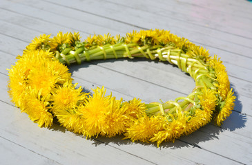 a wreath of yellow dandelion flowers on a gray wooden background. a concept of a country summer vacation