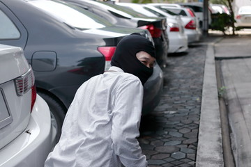 Masked burglar wearing a balaclava ready to burglary against car background. Insurance crime concept.