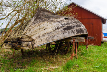 Ahus, Sweden. Small broken rowboat resting upside down outside a red shed.
