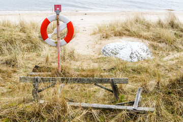 Fototapeta na wymiar Ahus, Sweden. Lifebuoy and sand covered lifeboat on a beach.