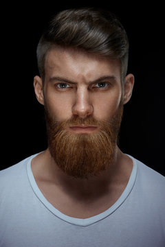 Close-up image of serious brutal bearded man on dark background in a white T-shirt Confident and dramatic concept