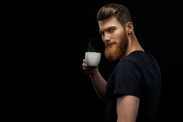 Cheerful professional handsome project manager in black t-shirt holding coffee cup drinking morning...